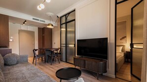 Una sala moderna con un sofá, televisión, comedor y un dormitorio visible a través de una puerta corrediza.