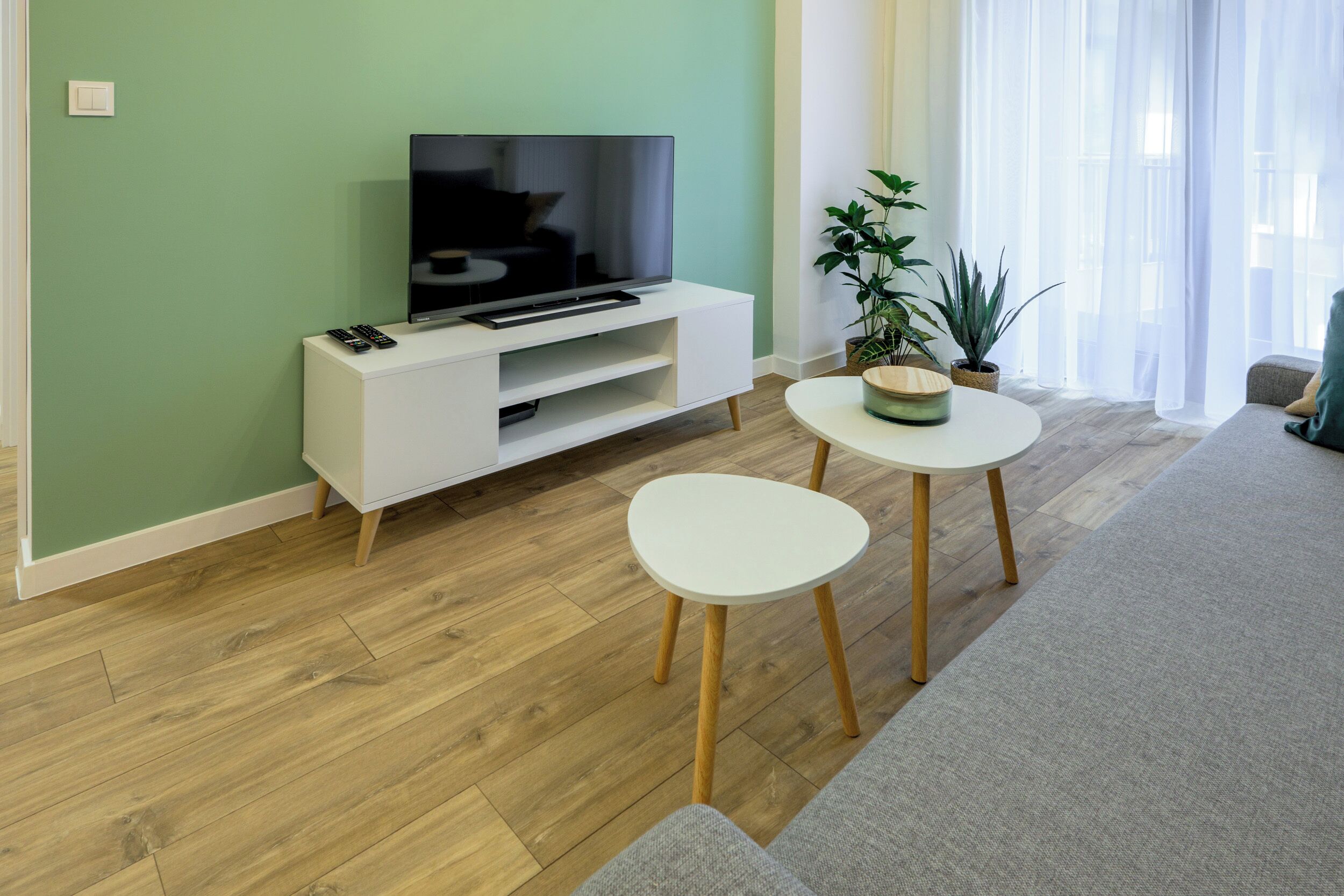 A modern living room with a flat-screen TV on a white entertainment unit, a round coffee table, and a grey sofa.