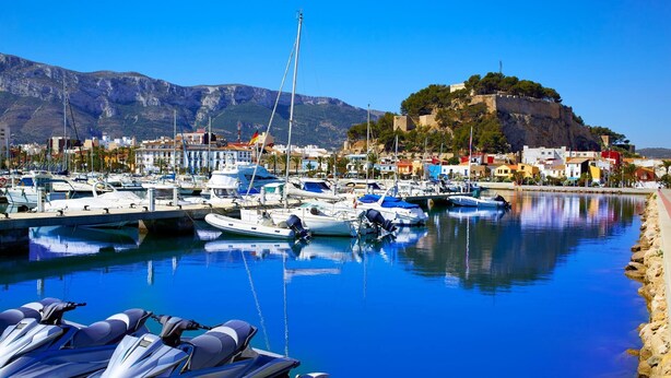 A marina with boats and jet skis, a rocky shoreline, and a hill with buildings in the background. - Private Pool, Garden, Barbecue and Beach Nearby (Denia)
