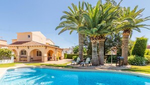 A swimming pool with lounge chairs, palm trees, and a Mediterranean-style building with arches. - Private Pool, Garden, Barbecue and Beach Nearby (Denia)