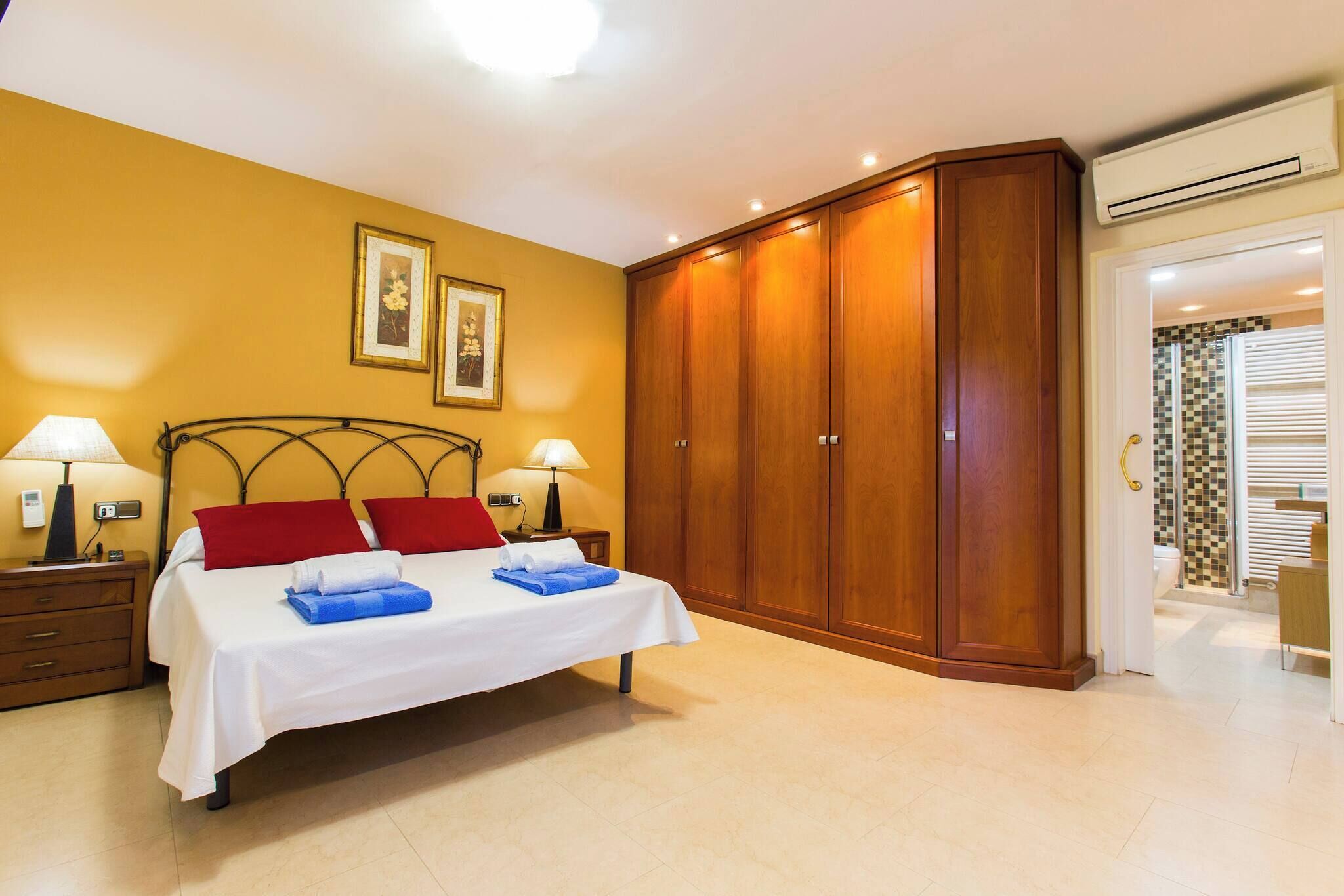 A bedroom with a bed, wooden wardrobe, two bedside lamps, and a nightstand.