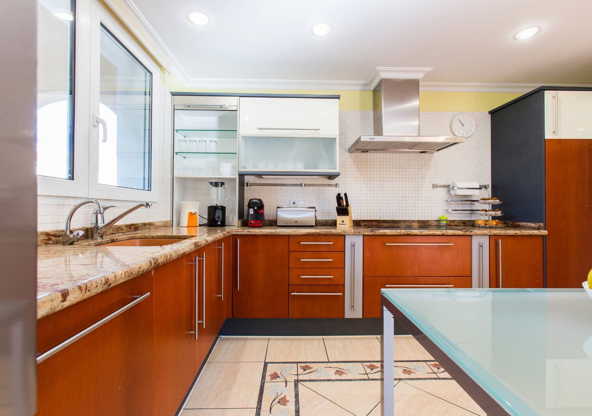 A modern kitchen with wooden cabinets, a glass-top table, and a built-in oven.