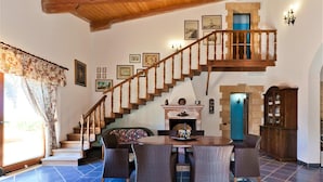 Un comedor con mobiliario de mimbre, una escalera de madera y una chimenea.