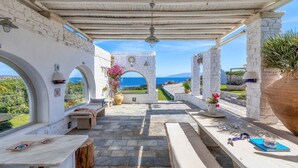 Ein überdachter Außenbereich mit Steinsäulen, Meerblick und einer Pergola.