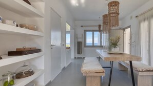 Eine moderne Küche mit weißen Schränken, einer zentralen Kochinsel, hängenden Lampen aus Makramee und Meerblick durch das Fenster.