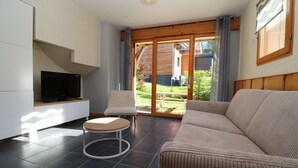 Een moderne woonkamer met een bank, een kleine ronde tafel, een televisie en een schuifdeur naar een tuin.