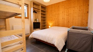 Een stapelbed met een houten ladder, een nachtkastje, een klein plankje en een wandplank met een hangende plant.