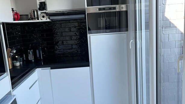 A modern kitchen with white cabinets, a black backsplash, and a built-in oven.