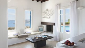 A room with a stone bench by a window overlooking the sea, a fireplace, and a table with apples. - My Rental Homes - Villa Elpida with infinity pool overlooking  the Aegean sea (Mykonos)