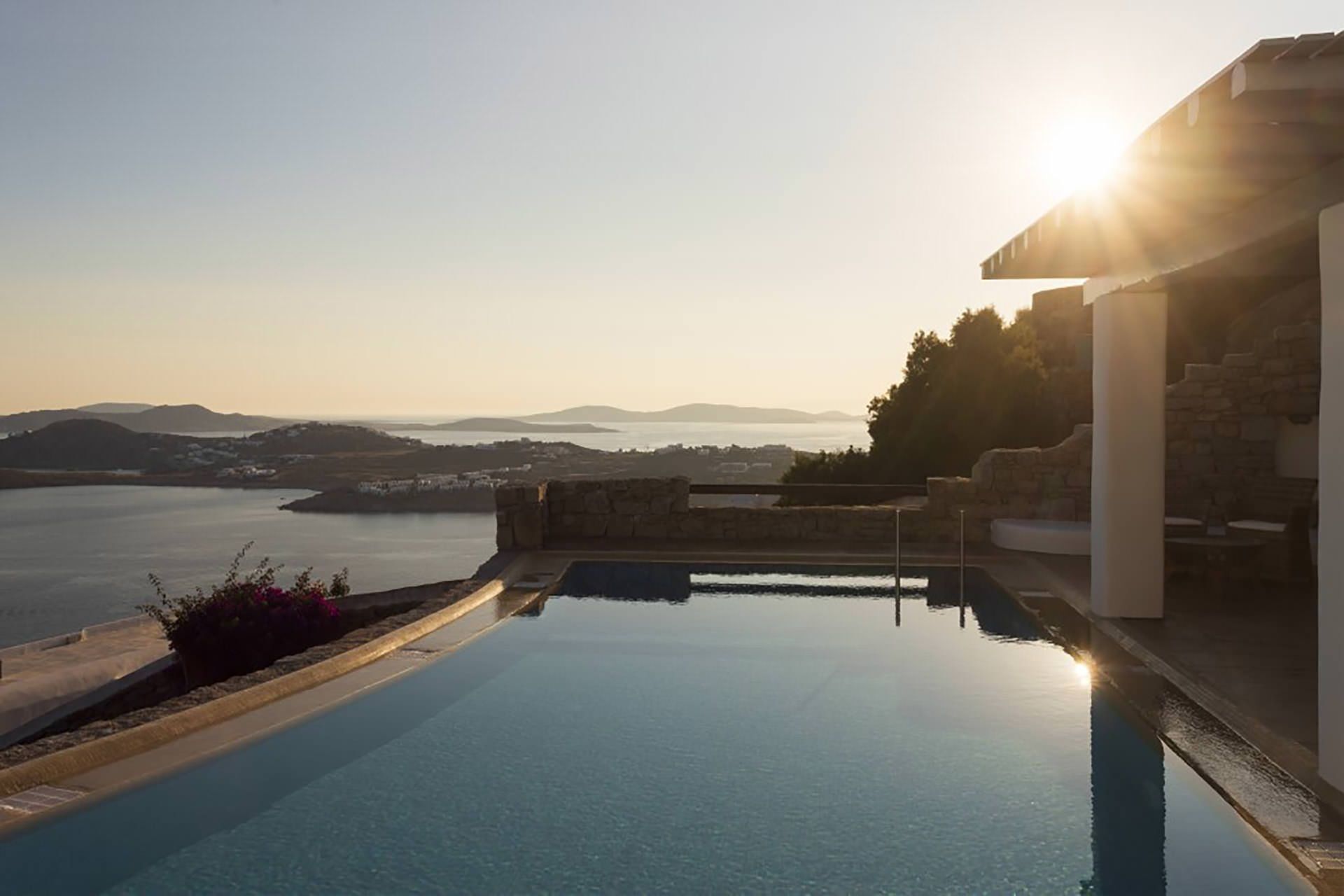 Vista chiara di una piscina con muretto in pietra e sullo sfondo mare e colline lontane.