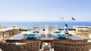A table set for four with blue plates, glasses, and a pitcher, overlooking the sea. - My Rental Homes - Villa Elpida with infinity pool overlooking  the Aegean sea (Mykonos)