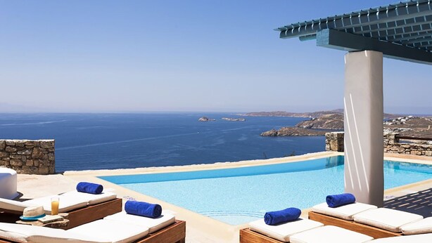 A poolside area with lounge chairs and a view of the sea. - My Rental Homes - Villa Elpida with infinity pool overlooking  the Aegean sea (Mykonos)