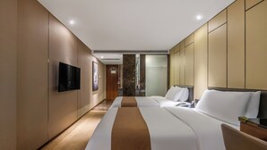 Habitación de hotel con dos camas, televisión de pantalla plana, minibar y baño con cabina de ducha de vidrio.