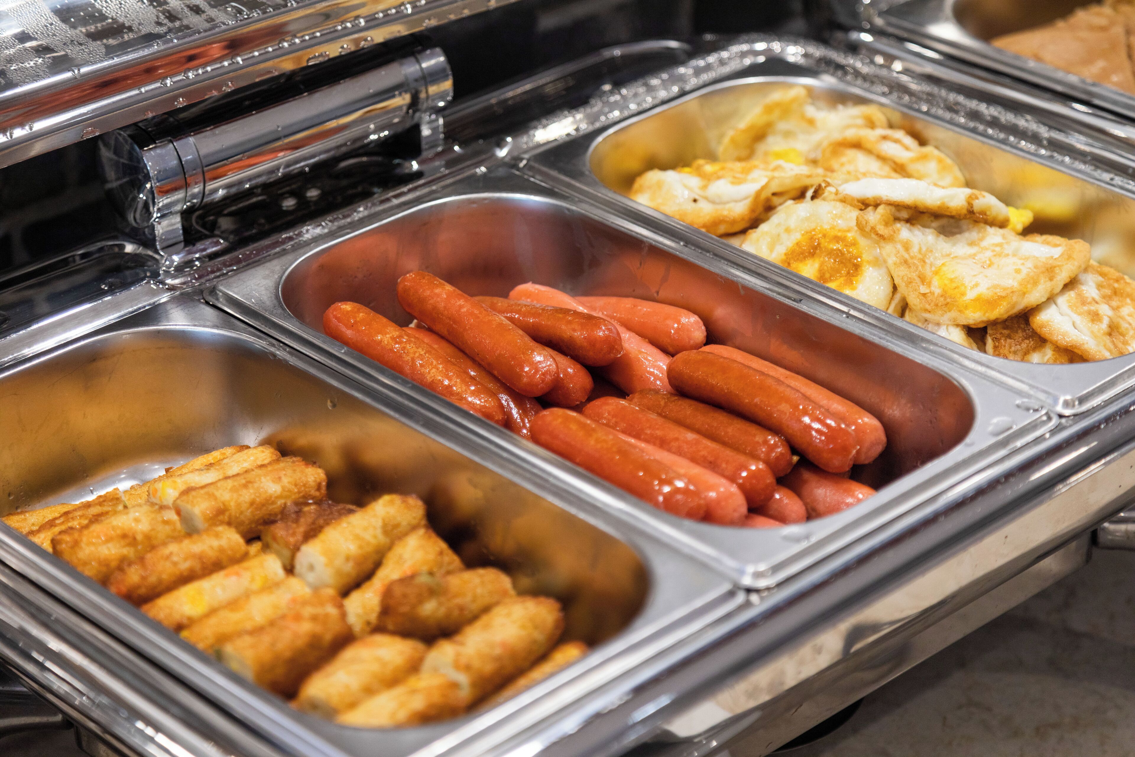 Un bufé con diferentes opciones de comida, incluyendo perros calientes, pollo frito y palitos de papa.