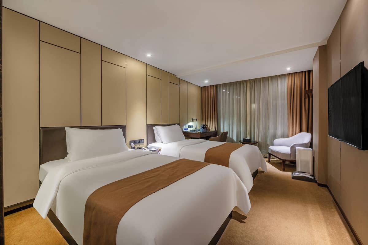 A hotel room with two beds, a desk, a chair, a TV, and a window with curtains.