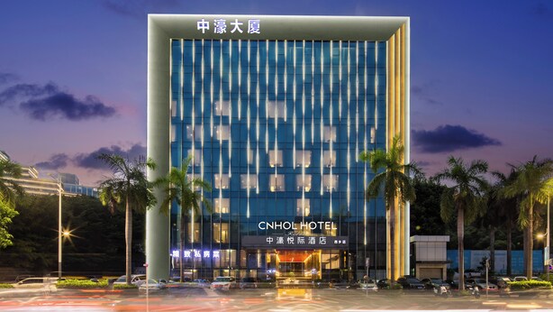 Un hotel moderno con un llamativo letrero CNHOL HOTEL, que presenta una fachada vertical con ventanas reflectantes y una entrada central.