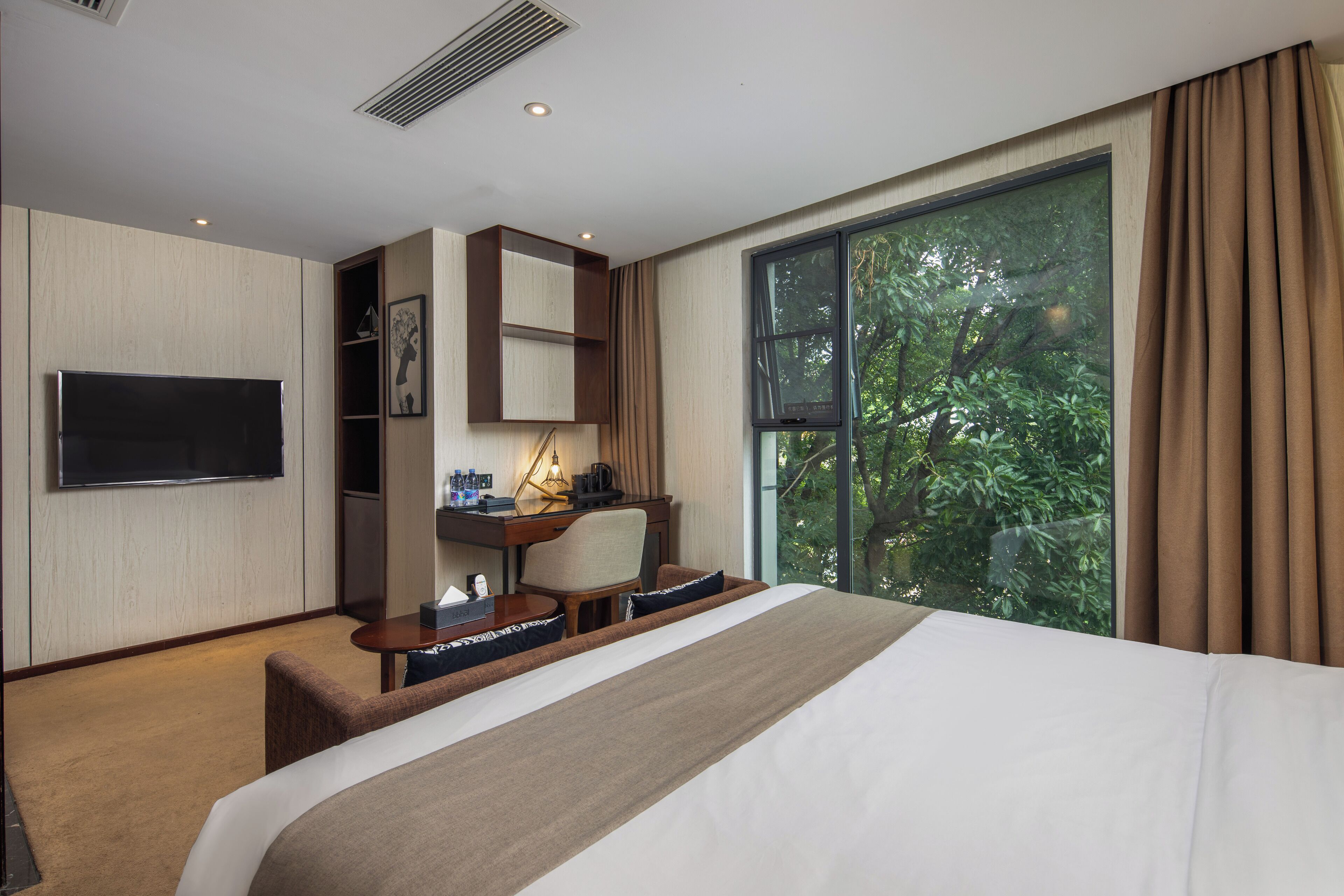 A hotel room with a large bed, a desk with a chair, a television, and a window with curtains.