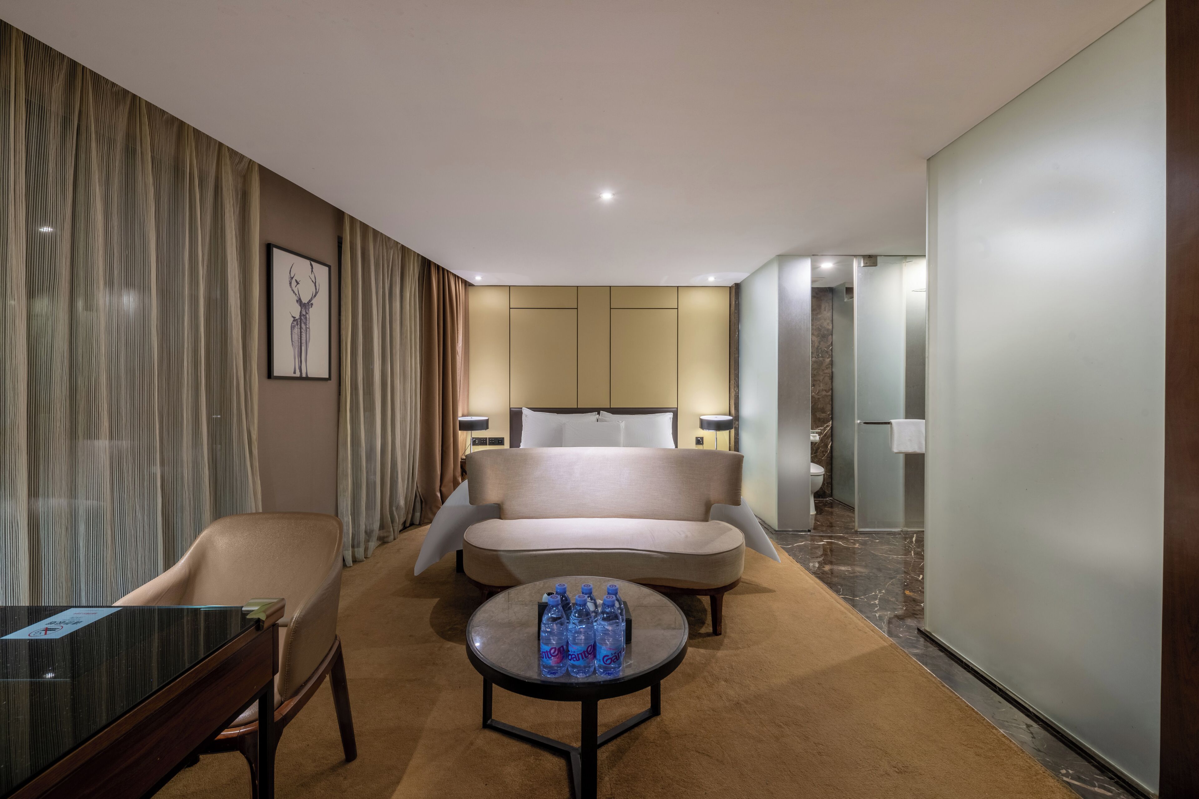 Une chambre d’hôtel comprenant un lit, un canapé, une table basse avec des bouteilles d’eau, un bureau et une chaise.