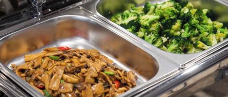 Buffet com duas bandejas de metal, uma com noodles refogados e outra com brócolis cozido no vapor.