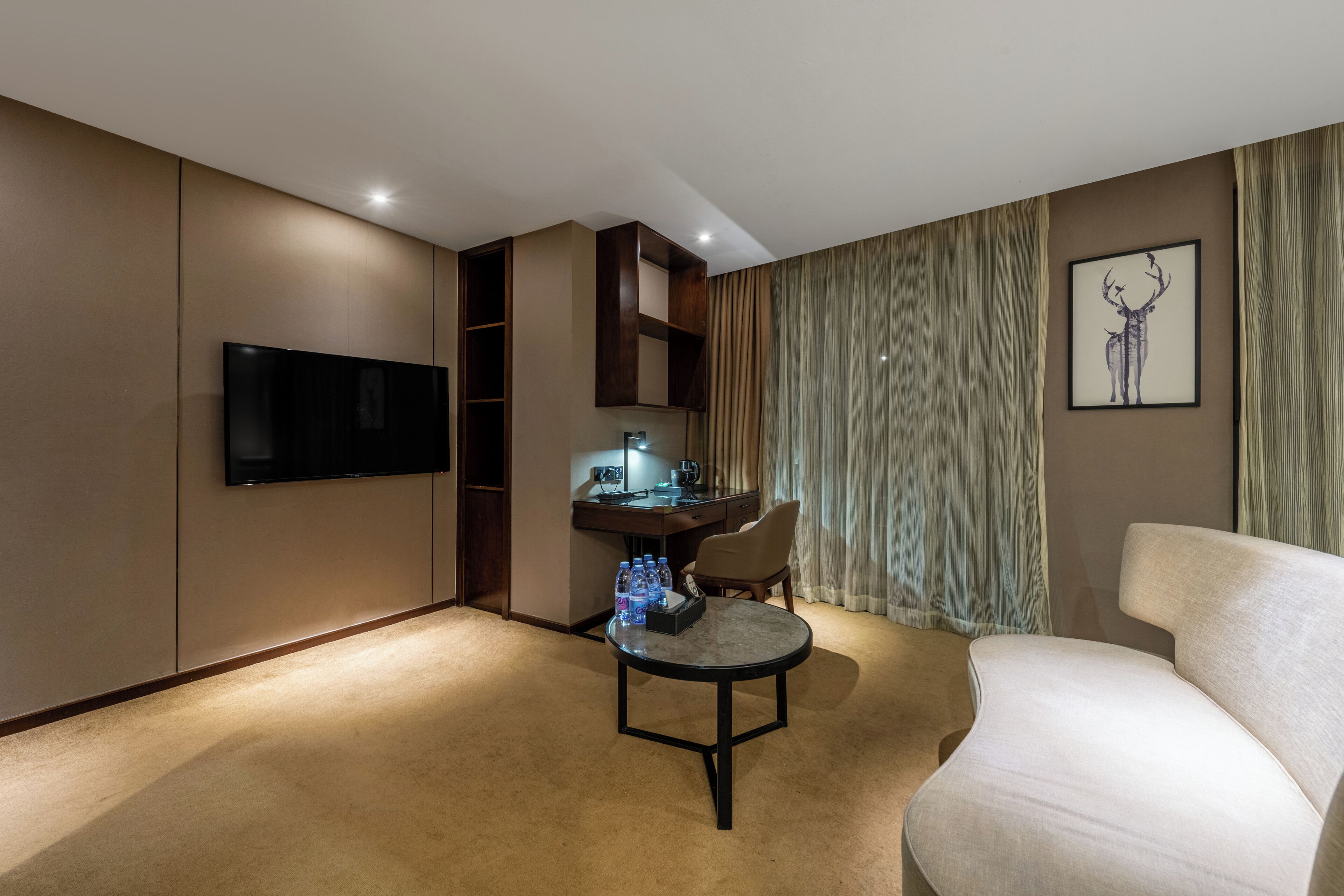 A hotel room with a flat-screen TV, a desk with a computer, a chair, a sofa, and a framed picture on the wall.