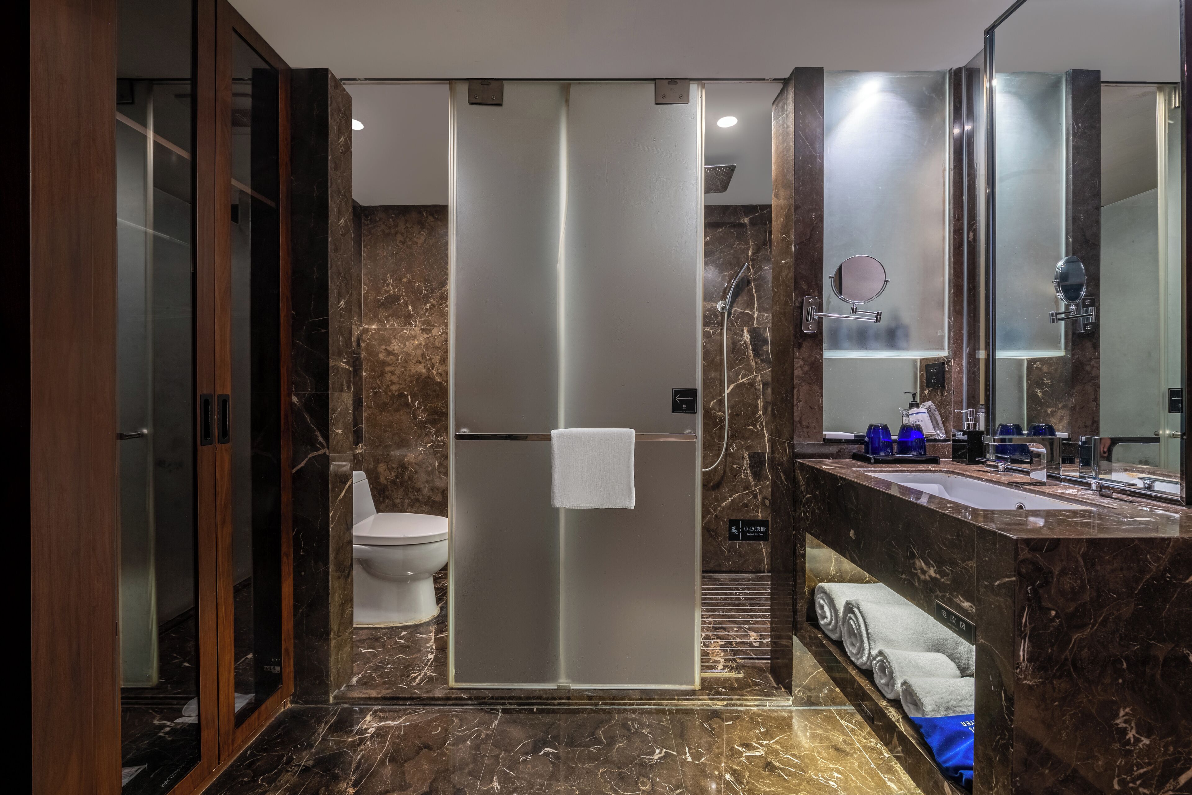 A modern bathroom with a glass shower enclosure, a marble-topped sink, and a large mirror.