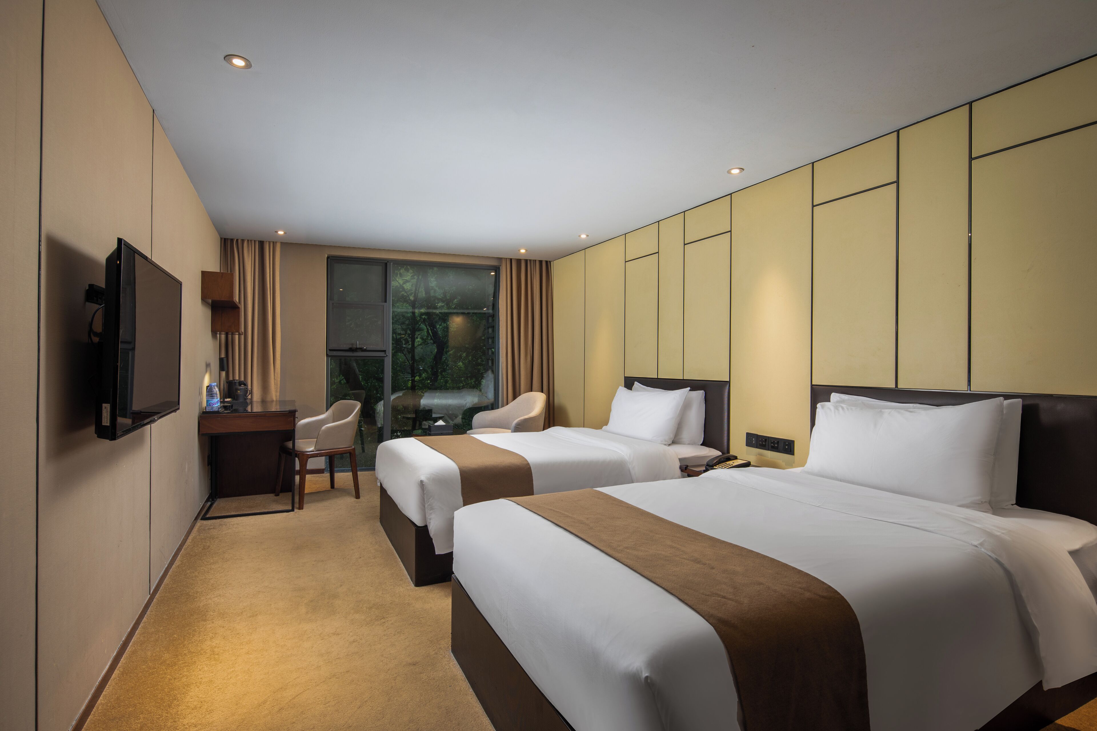 A hotel room with two beds, a desk, a chair, and a TV.