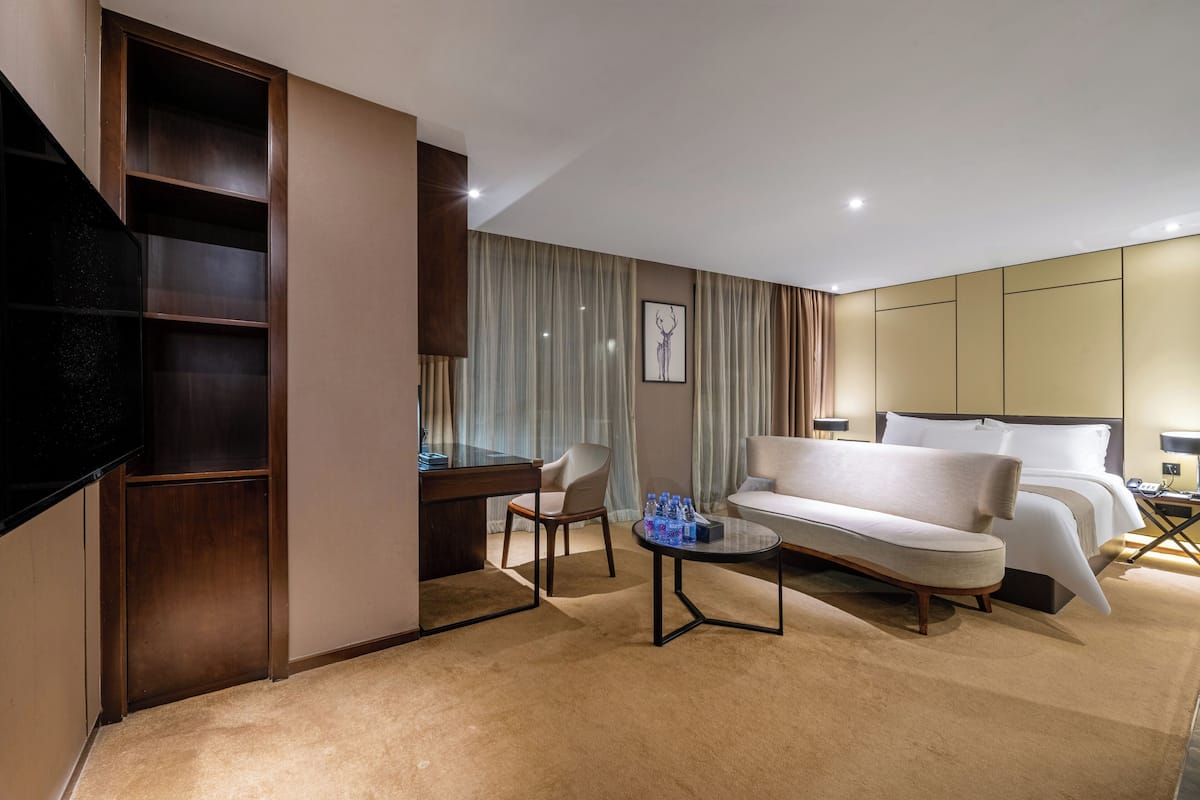 A hotel room with a bed, a sofa, a desk, and a television.
