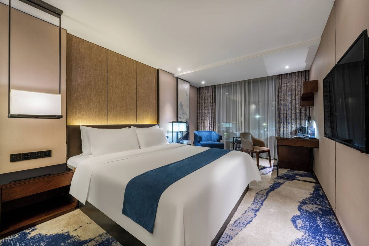 A modern hotel room with a large bed, a desk, a chair, and a TV.
