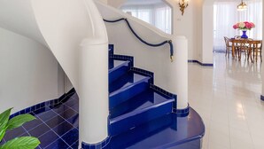 Eine Treppe mit blauen Stufen und weißen Wänden führt zu einem Essbereich mit einer Kristallleuchter und einem Tisch mit Stühlen.