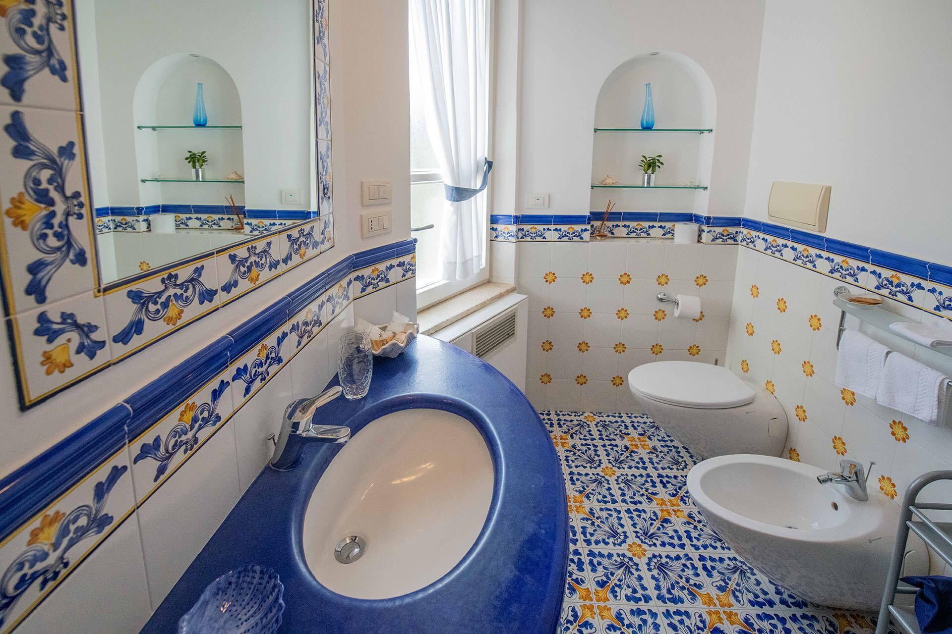 Une salle de bain avec un sol carrelé de bleu et de blanc, un grand lavabo, des toilettes et un miroir.