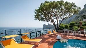 Ein Poolbereich mit Liegestühlen, einem Tisch und Blick auf das Meer.