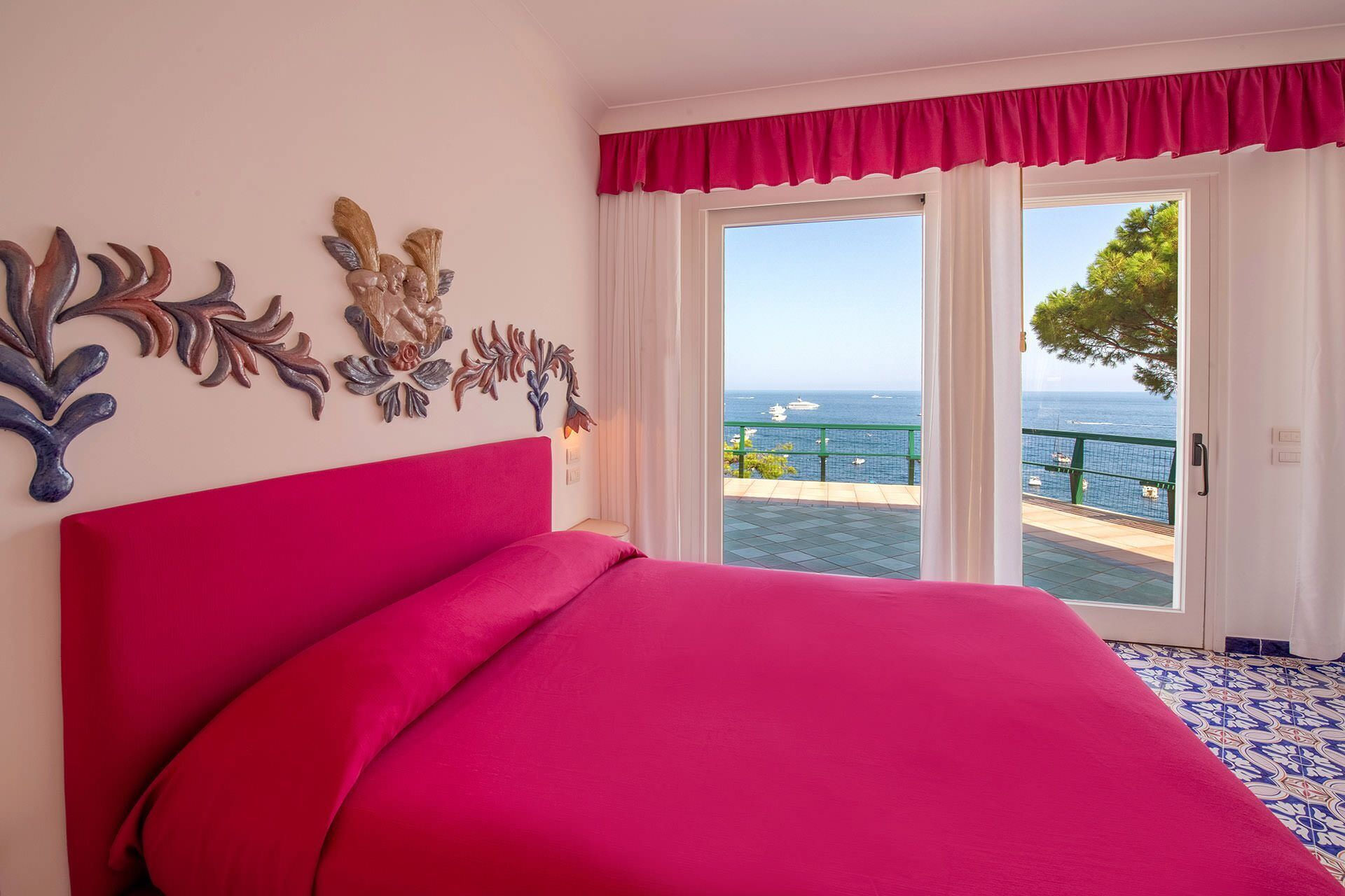 Ein Zimmer mit einem großen Bett, einem Balkon mit Meerblick und dekorativen Wandbildern.