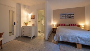 Ein Schlafzimmer mit Bett, Nachttischen, einem Schminktisch, einem Schrank und einem durch eine offene Tür einsehbaren Badezimmer.