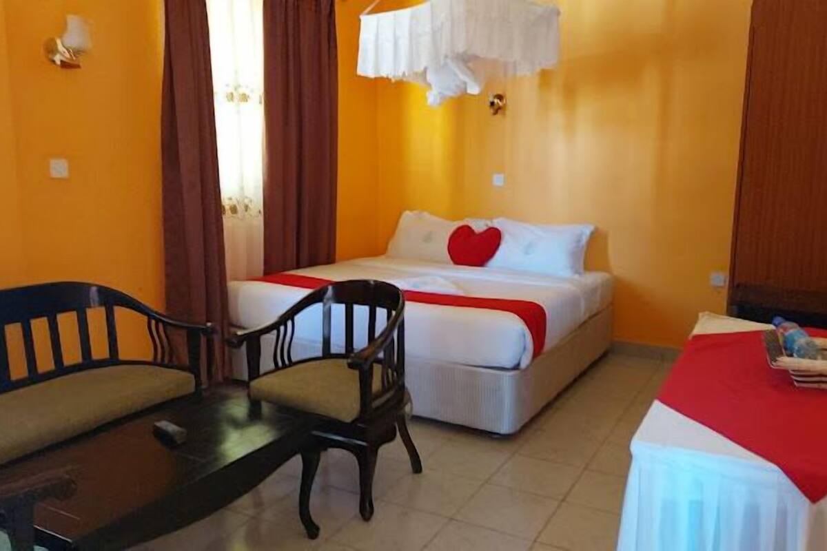 A hotel room with a bed, a chair, a small table, and a window with curtains.