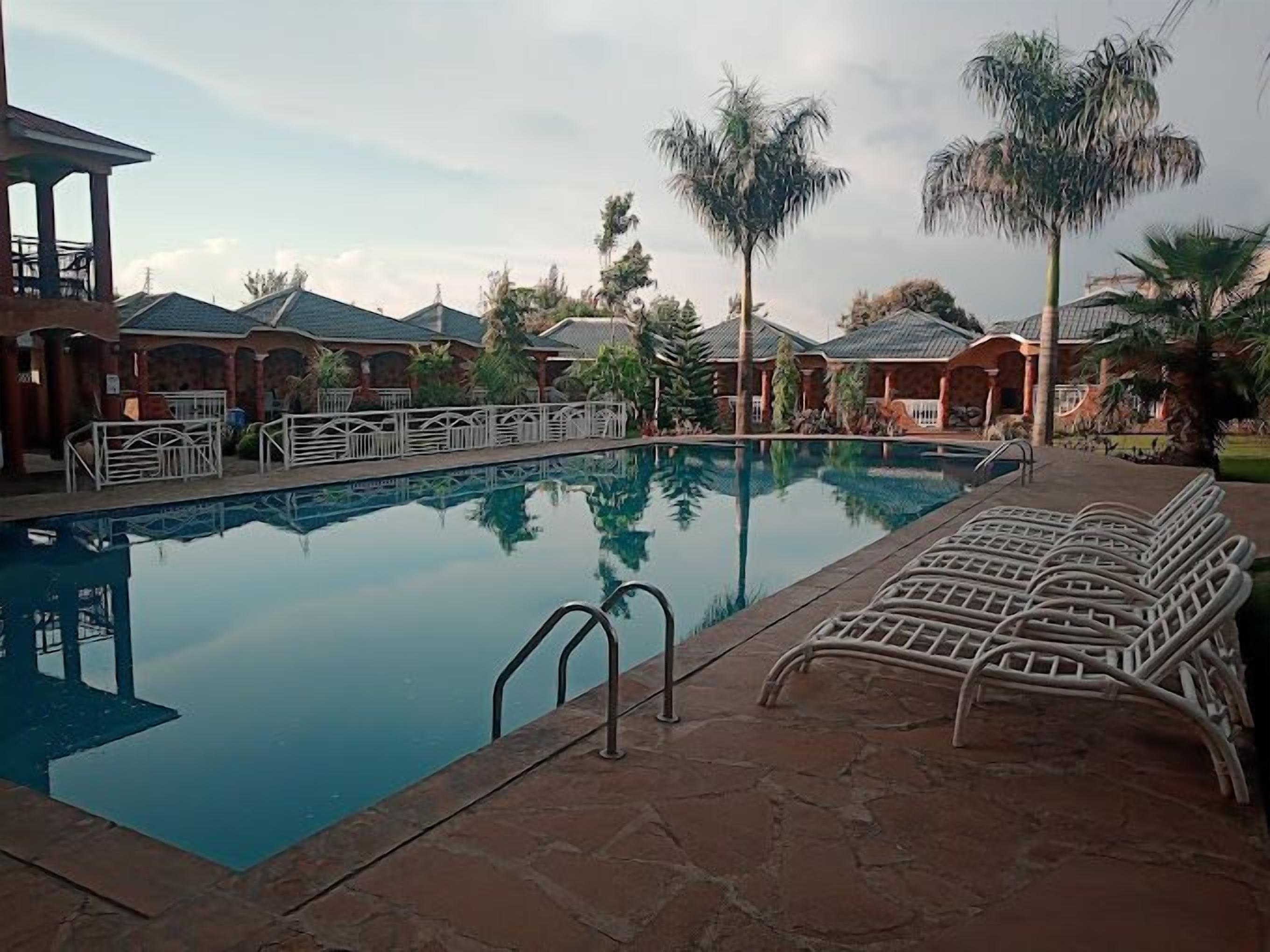 A swimming pool with lounge chairs, palm trees, and covered structures.