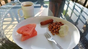A plate with food items including a sausage, beans, and a piece of bread, accompanied by a cup of coffee on a glass table.