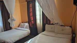 Ένα δωμάτιο ξενοδοχείου με δύο κρεβάτια, ένα κρεβάτι με ουρανό και ένα παράθυρο με κουρτίνες.