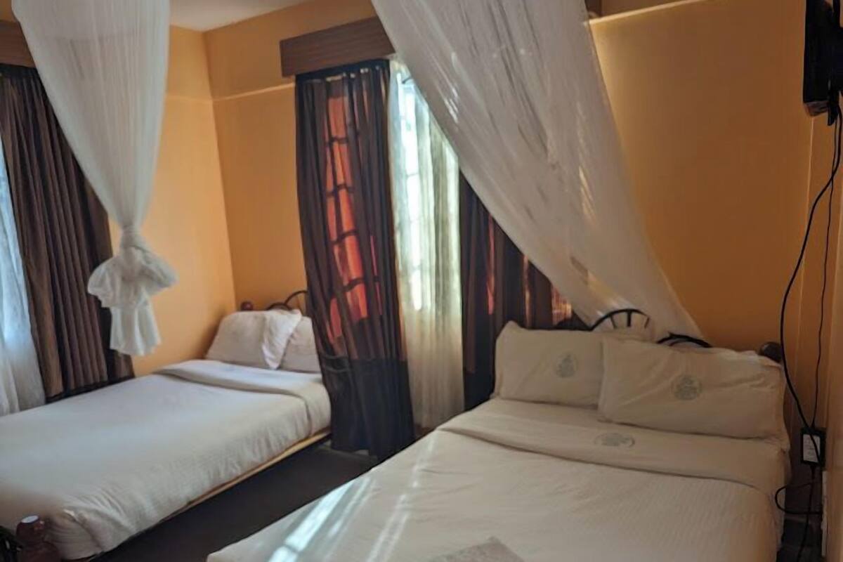 A hotel room with two beds, a canopy bed, and a window with curtains.