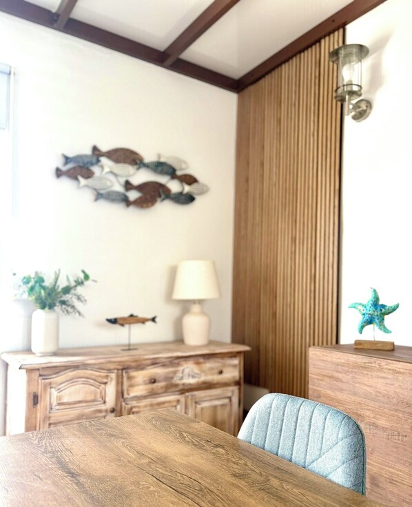 Un comedor con una mesa y sillas de madera, un aparador de madera con una lámpara, y una decoración de peces montada en la pared.