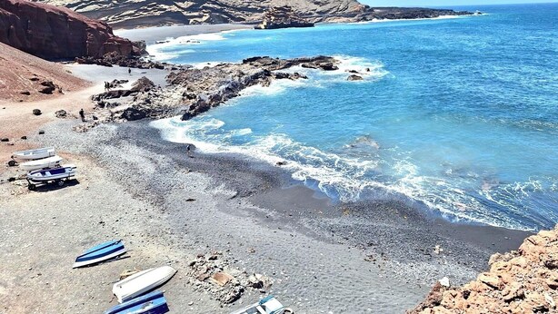 A rocky beach with boats and a mountainous backdrop.