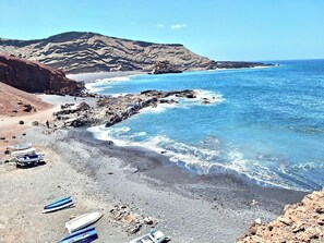 Una playa rocosa con barcos y montañas al fondo.