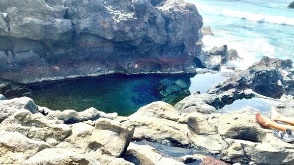A rocky coastal area with clear water and a person sitting on the rocks.