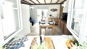 A bright room with a wooden ceiling, a dining table set for four, and a kitchen area visible through an open door.