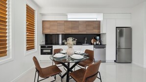 Une cuisine moderne avec un coin repas, comprenant un réfrigérateur en acier inoxydable, une cuisinière noire et des armoires en bois.