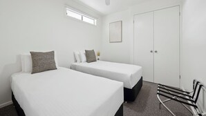 Une chambre d’hôtel avec deux lits simples, un ventilateur de plafond, une fenêtre, une porte et une petite plante.