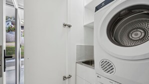 Une petite buanderie blanche, équipée d’un lave-linge à chargement frontal, d’un sèche-linge et d’un petit évier.
