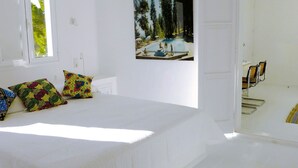 Un dormitorio con cama, almohadas coloridas, un cuadro de una piscina y una puerta que da a un baño.