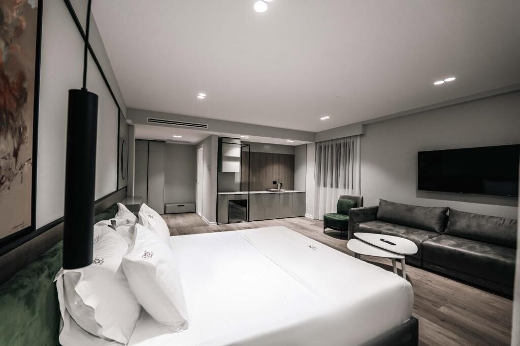 A modern hotel room with a large bed, a sofa, a TV, and a small table.