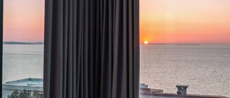 A room with a view of the sunset over the water, a table, and two chairs.
