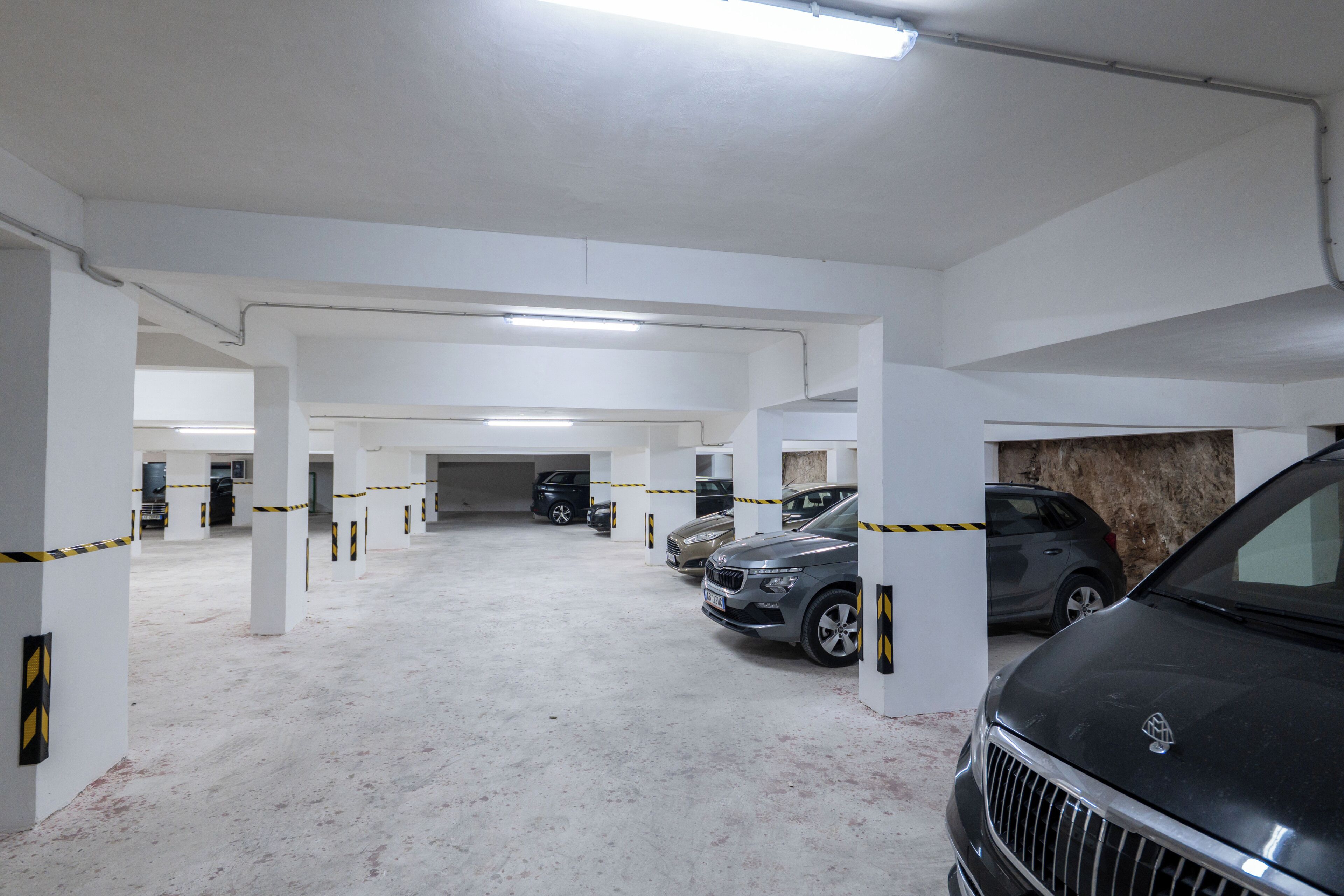 Eine mehrstöckige Parkgarage mit weißen Säulen, gelbem Absperrband und mehreren parkenden Autos.